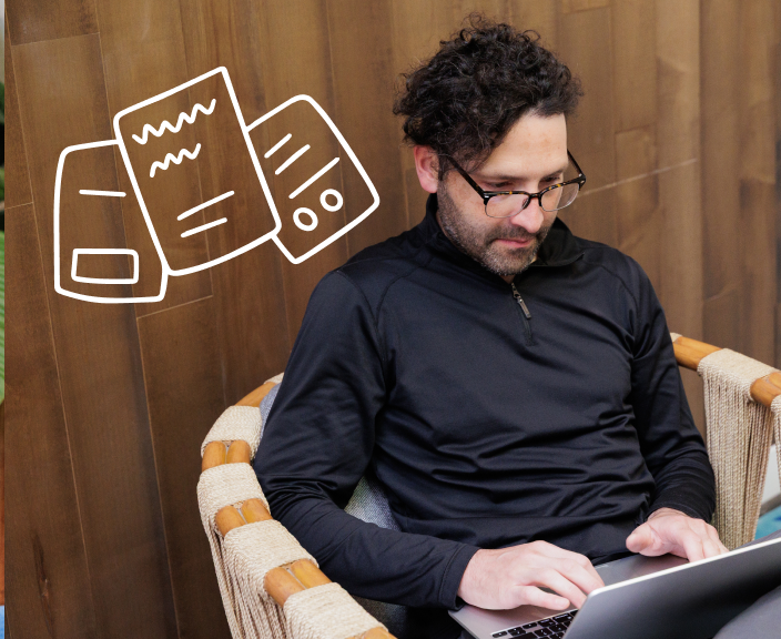 Man with curly hair and glasses working on laptop while sitting in wicker chair, with illustrated document icons floating nearby