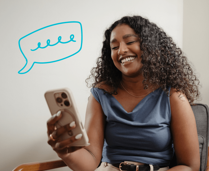 Woman with curly hair smiling while looking at her phone with a speech bubble containing wavy lines above