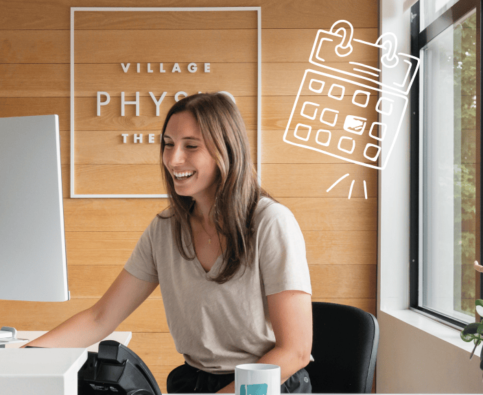 Smiling woman in beige shirt sitting at desk in modern office with wood paneling and Village Physio branding