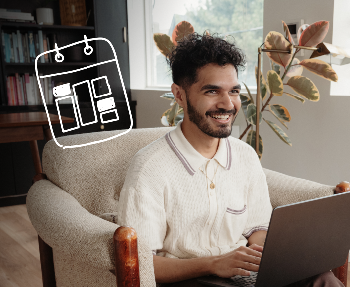 Man with curly hair and beard smiling while using laptop in living room with calendar icon overlay