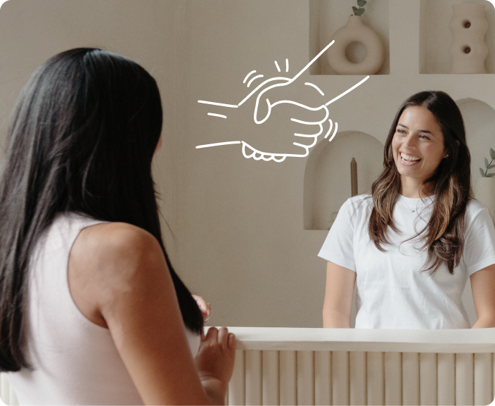 Two women at a reception desk with illustrated handshake symbol between them representing partnership or agreement