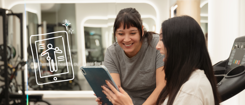Trainer and client smiling while reviewing a workout plan on a tablet in a gym