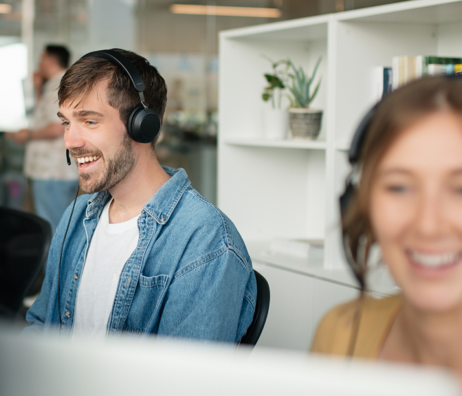 Smiling customer service agents wearing headsets working at desks in an office