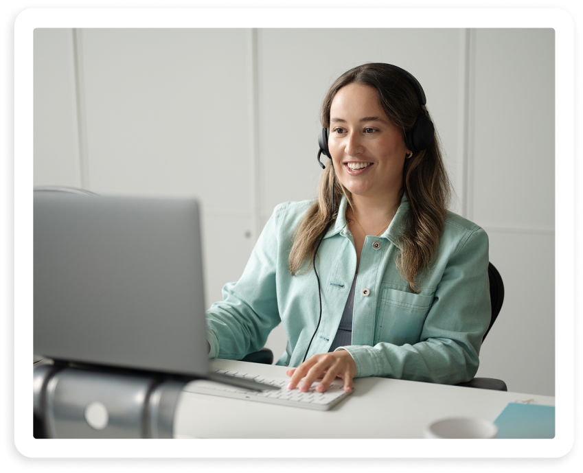 Woman wearing a headset smiling while working at a laptop and keyboard
