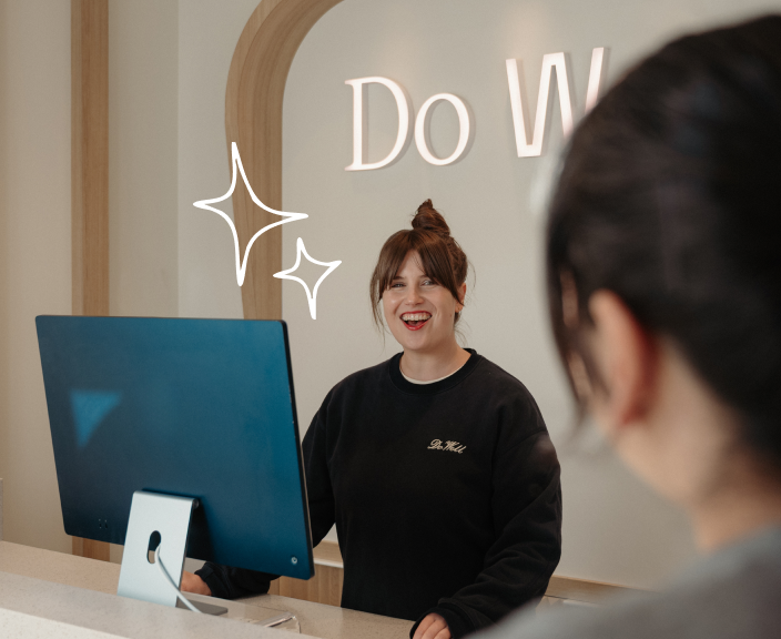 Smiling receptionist greeting a customer at the front desk of a Do Well studio