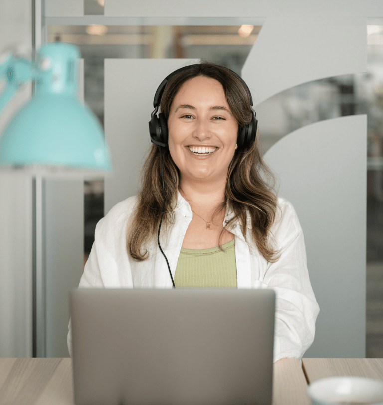 Woman wearing headphones smiling at a laptop in an office setting