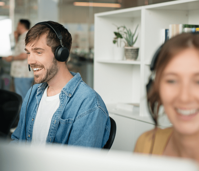 Smiling customer service agents wearing headsets working at desks in an office